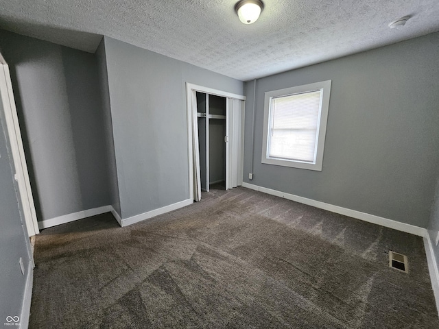 unfurnished bedroom with visible vents, a textured ceiling, a closet, dark colored carpet, and baseboards