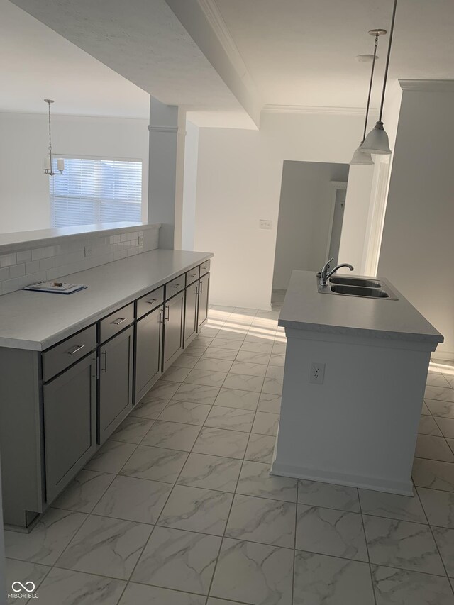 kitchen with a sink, marble finish floor, ornamental molding, and pendant lighting