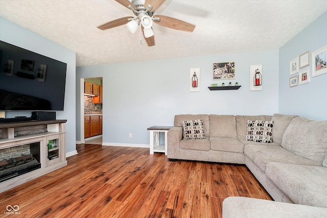 living area featuring a ceiling fan, a textured ceiling, a fireplace, baseboards, and dark wood-style flooring