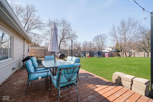 wooden deck featuring a trampoline, a fenced backyard, a playground, a yard, and outdoor dining area