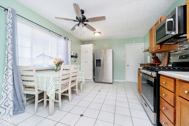 kitchen featuring light countertops, brown cabinets, appliances with stainless steel finishes, light tile patterned flooring, and a ceiling fan