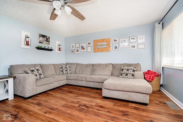 living room with visible vents, ceiling fan, baseboards, wood finished floors, and a textured ceiling