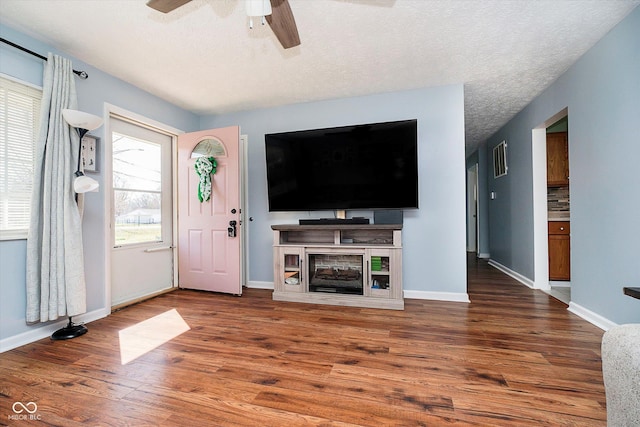 unfurnished living room featuring visible vents, baseboards, wood finished floors, a textured ceiling, and a ceiling fan