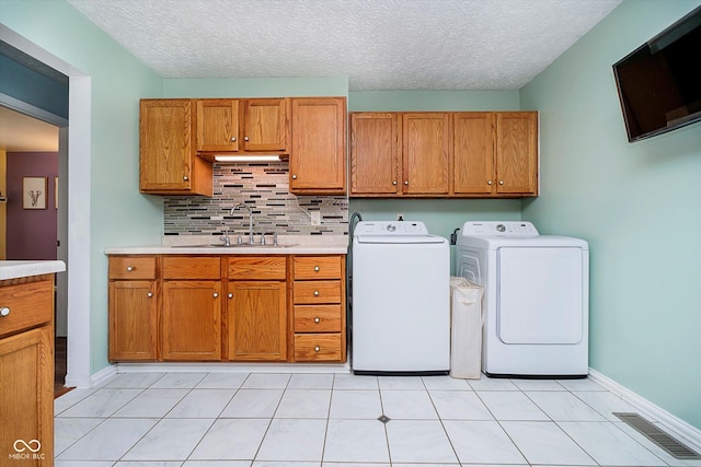 clothes washing area featuring visible vents, a sink, washer and dryer, cabinet space, and baseboards