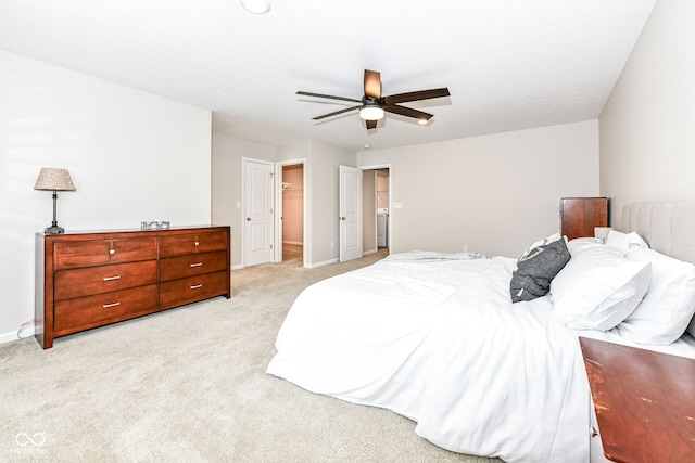 bedroom with a walk in closet, light colored carpet, baseboards, and ceiling fan