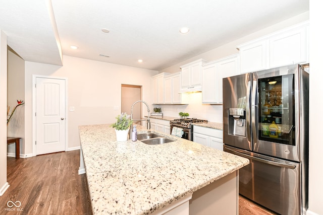 kitchen with wood finished floors, an island with sink, a sink, white cabinets, and appliances with stainless steel finishes