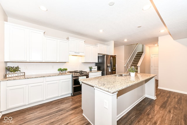 kitchen with a sink, under cabinet range hood, dark wood finished floors, stainless steel appliances, and a kitchen island with sink