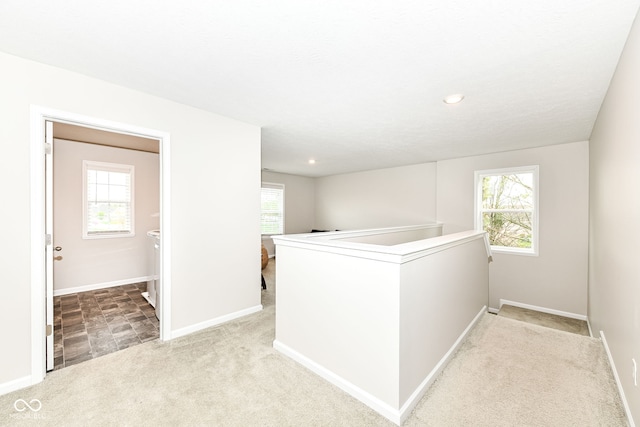 hall with an upstairs landing, baseboards, and carpet floors