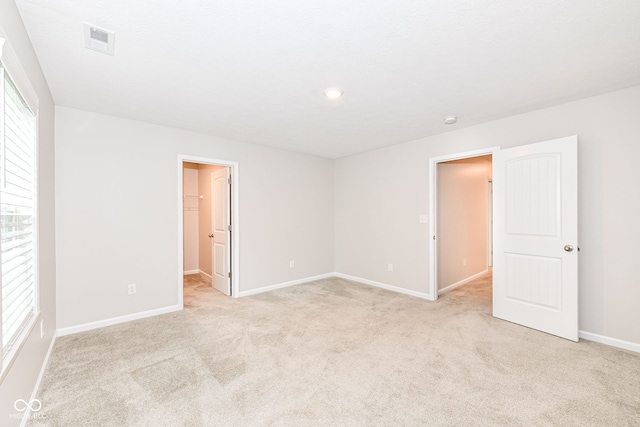 unfurnished bedroom featuring a spacious closet, multiple windows, visible vents, and light carpet