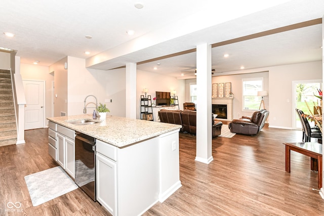 kitchen with light stone countertops, light wood-type flooring, a sink, a glass covered fireplace, and open floor plan