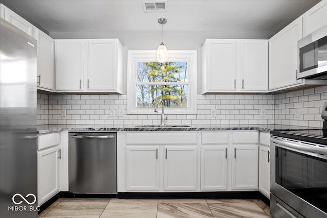 kitchen with a sink, stone countertops, tasteful backsplash, stainless steel appliances, and white cabinets