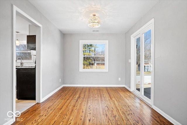 unfurnished dining area with visible vents, a sink, baseboards, and wood finished floors