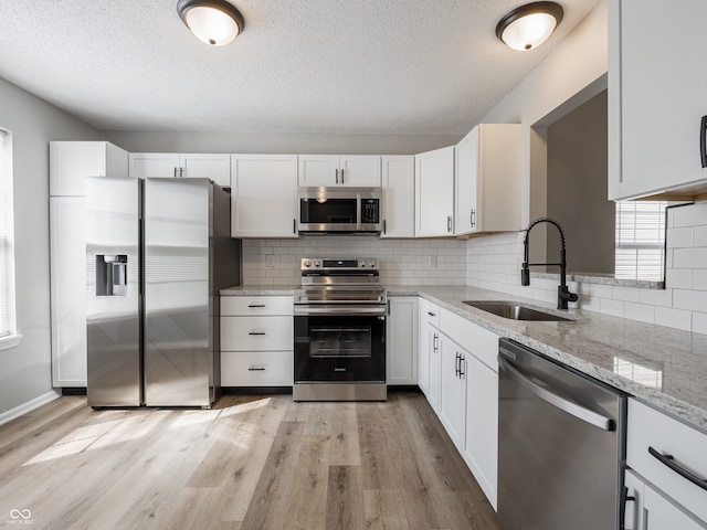 kitchen featuring light stone counters, stainless steel appliances, light wood-style floors, white cabinetry, and a sink