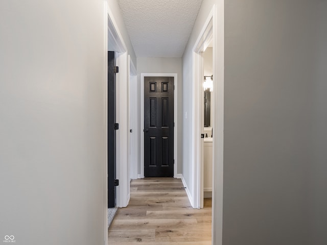 corridor featuring light wood-style floors and a textured ceiling