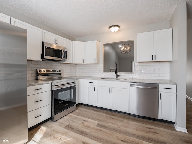 kitchen with light wood finished floors, a sink, white cabinets, appliances with stainless steel finishes, and tasteful backsplash