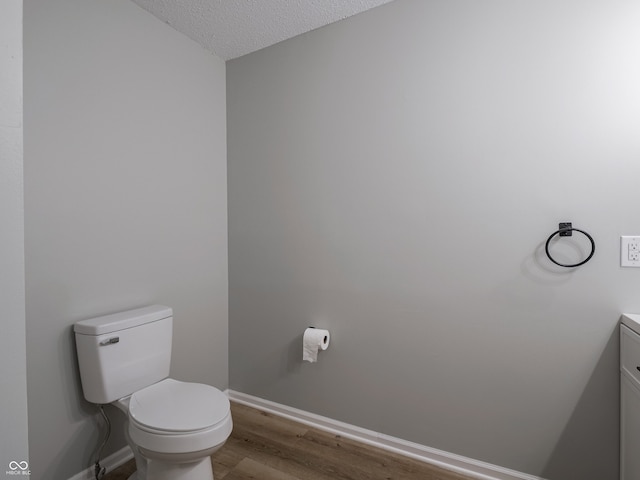 bathroom with toilet, a textured ceiling, wood finished floors, baseboards, and vanity