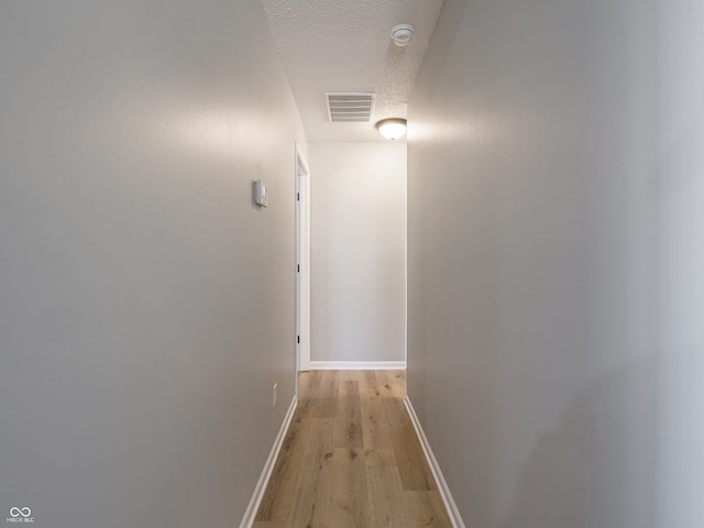 corridor with baseboards, visible vents, a textured ceiling, and light wood-style floors