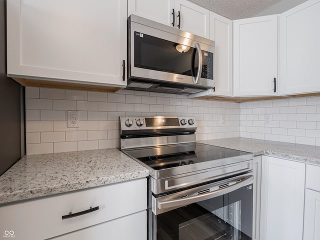 kitchen featuring tasteful backsplash, white cabinets, appliances with stainless steel finishes, and light stone counters