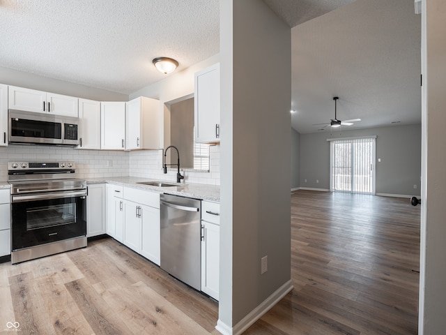 kitchen featuring light wood finished floors, backsplash, stainless steel appliances, white cabinetry, and a sink