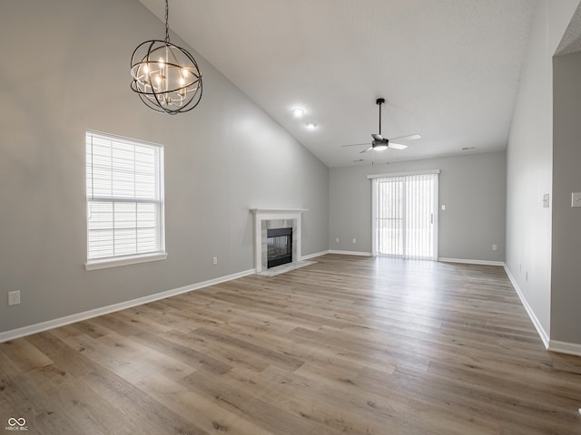 unfurnished living room with baseboards, high vaulted ceiling, a tile fireplace, ceiling fan with notable chandelier, and light wood-type flooring