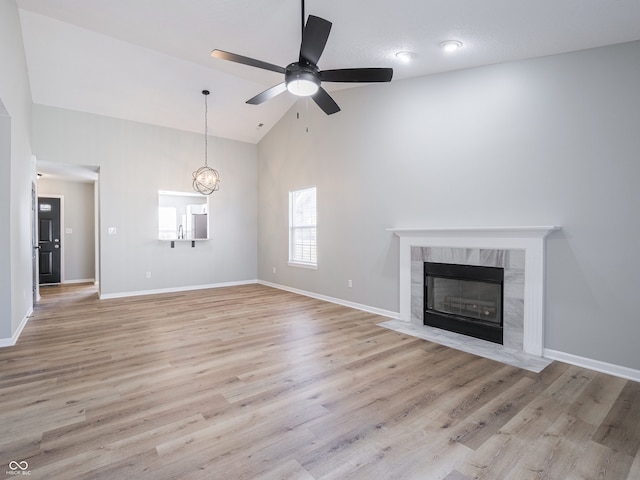 unfurnished living room featuring high vaulted ceiling, a ceiling fan, light wood finished floors, a premium fireplace, and baseboards