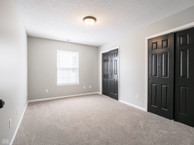 unfurnished bedroom featuring visible vents, a textured ceiling, a closet, carpet floors, and baseboards