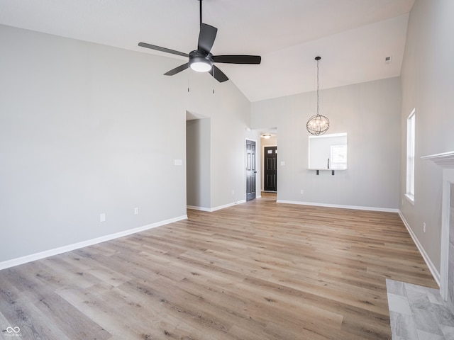 unfurnished living room with baseboards, light wood finished floors, high vaulted ceiling, a premium fireplace, and ceiling fan with notable chandelier