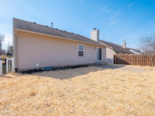 back of house featuring entry steps, a chimney, a yard, and fence