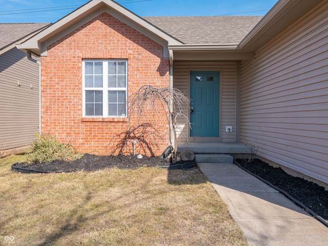 property entrance featuring brick siding, a lawn, and roof with shingles