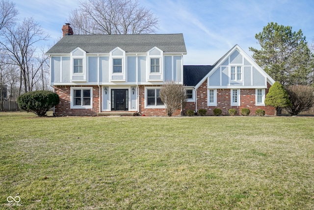 view of front facade with brick siding, a chimney, a front yard, and roof with shingles