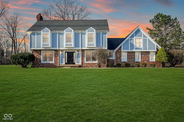 view of front of house with brick siding, a chimney, a front lawn, and a shingled roof