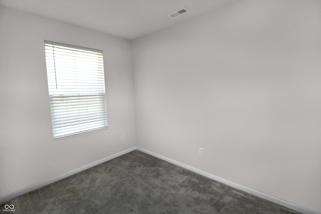 spare room with baseboards, visible vents, and dark colored carpet