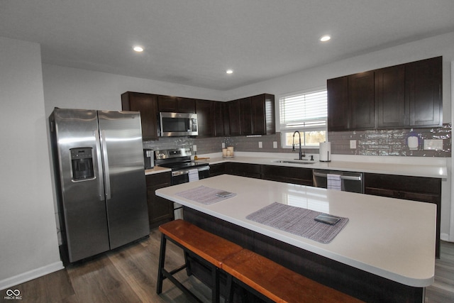 kitchen featuring backsplash, dark brown cabinets, dark wood-type flooring, appliances with stainless steel finishes, and a sink