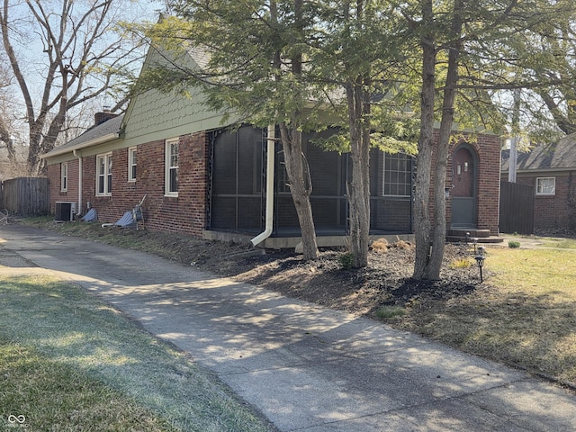 view of front of house with cooling unit, brick siding, a sunroom, and a chimney