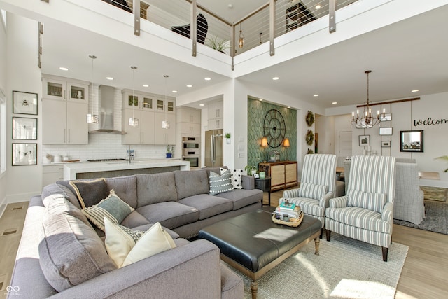 living room with a notable chandelier, recessed lighting, light wood-type flooring, and a towering ceiling