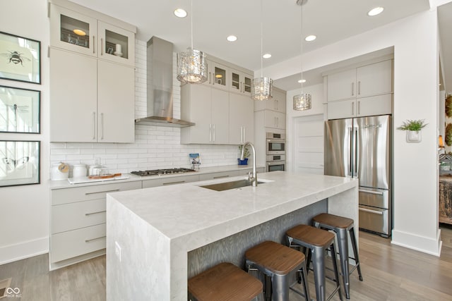 kitchen featuring a sink, wall chimney range hood, backsplash, and stainless steel appliances