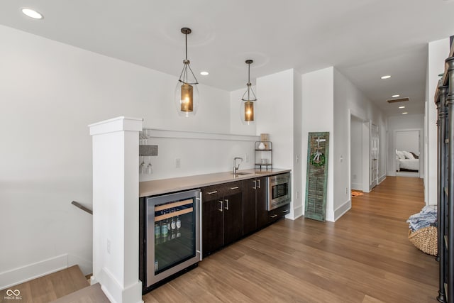 bar with wood finished floors, recessed lighting, indoor wet bar, hanging light fixtures, and wine cooler