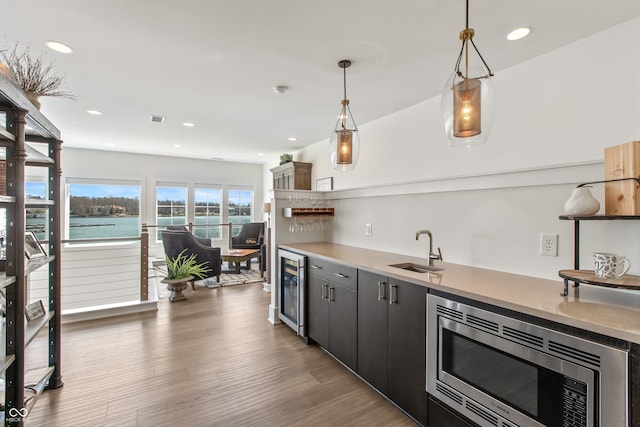 kitchen with wood finished floors, a sink, wine cooler, stainless steel microwave, and decorative light fixtures