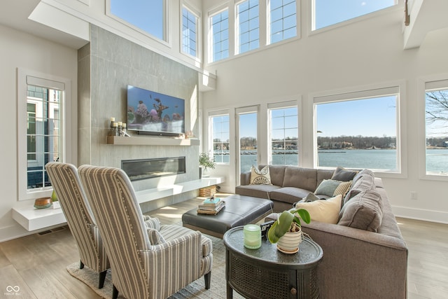 living area featuring visible vents, baseboards, a high ceiling, wood finished floors, and a glass covered fireplace