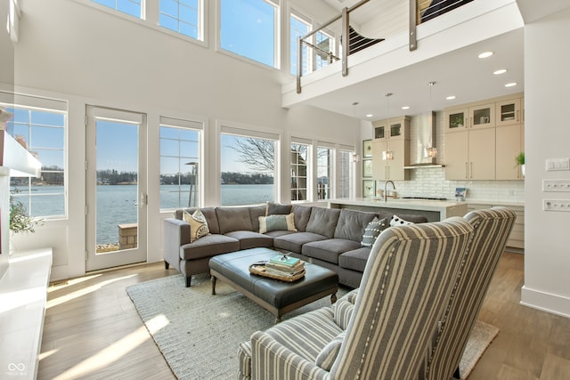 living area featuring recessed lighting, a water view, a towering ceiling, and wood finished floors