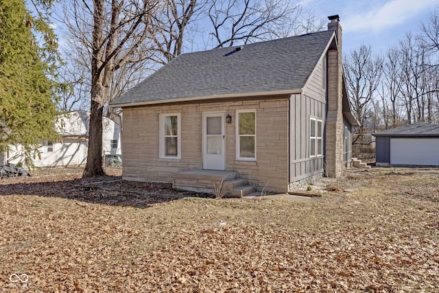 bungalow with stone siding, an outbuilding, a chimney, and a shingled roof