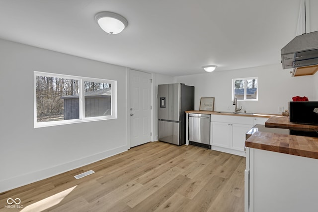 kitchen featuring butcher block countertops, light wood-style flooring, appliances with stainless steel finishes, white cabinets, and a sink