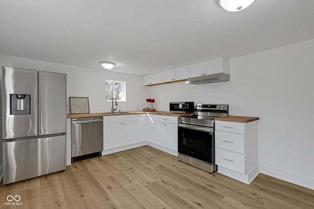 kitchen featuring light wood-style flooring, stainless steel appliances, white cabinets, under cabinet range hood, and wood counters