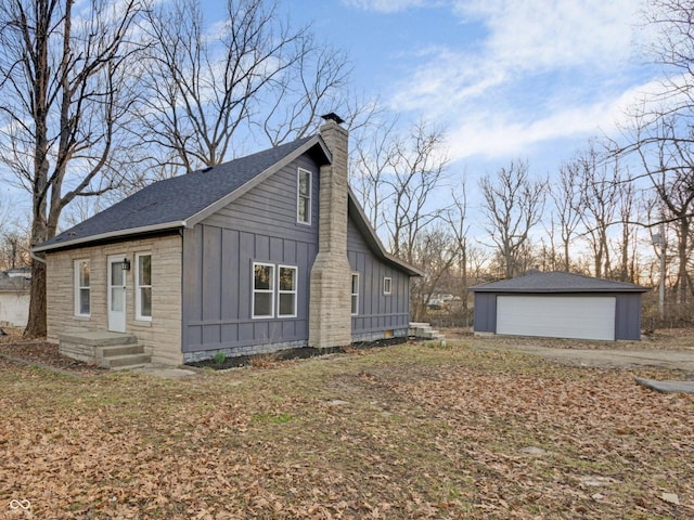 view of side of property with board and batten siding, roof with shingles, a chimney, a garage, and an outbuilding