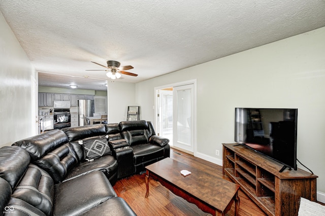 living area featuring visible vents, a ceiling fan, a textured ceiling, wood finished floors, and baseboards