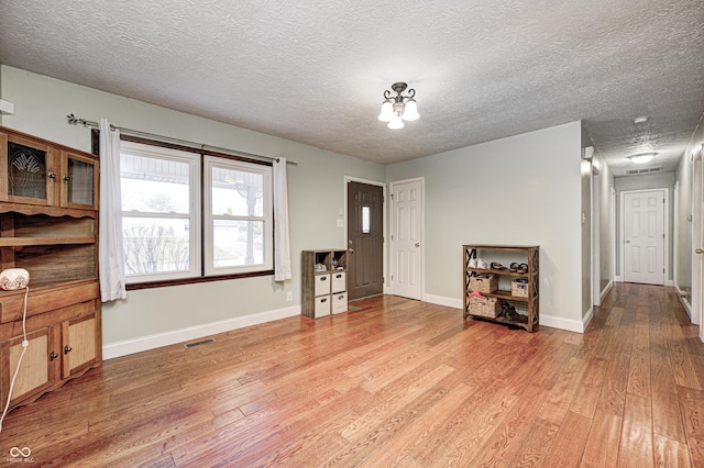 living area with visible vents, baseboards, a textured ceiling, and light wood-style flooring