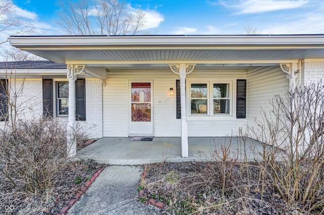 view of exterior entry featuring a porch and brick siding