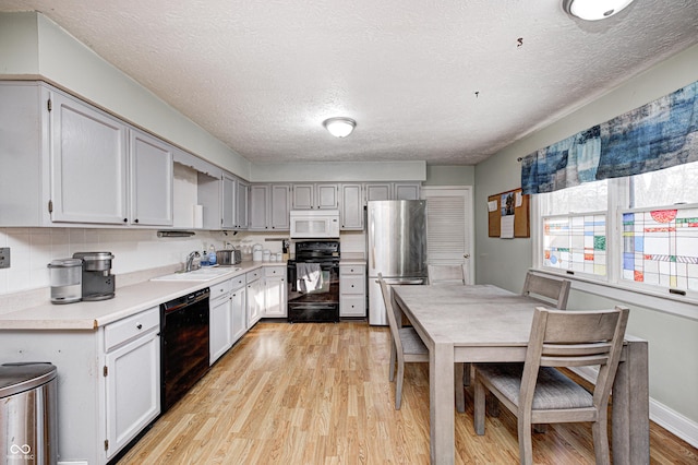 kitchen with light wood-style flooring, a sink, black appliances, light countertops, and tasteful backsplash