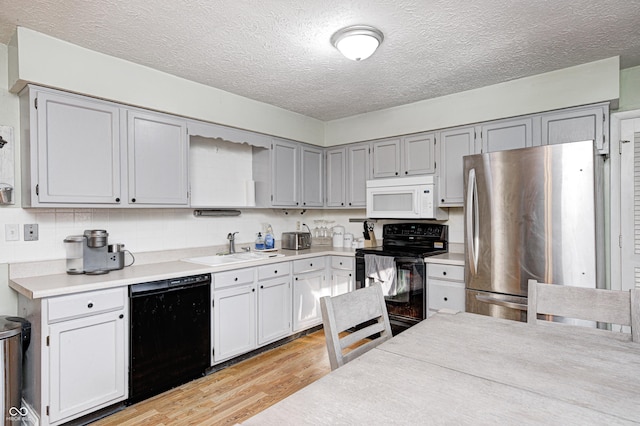 kitchen with light wood-type flooring, black appliances, a sink, a textured ceiling, and light countertops