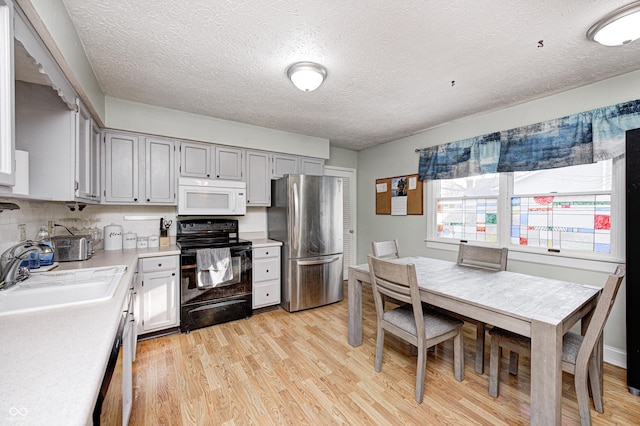 kitchen with white microwave, light countertops, freestanding refrigerator, electric range, and a sink